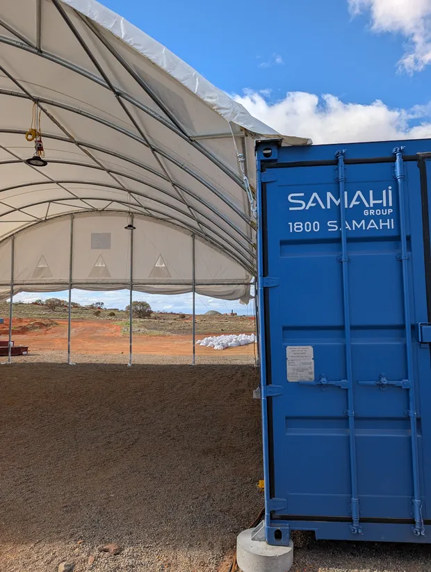 Inside a dome shelter looking out, with lighting hung from the frame and a container on precast footings